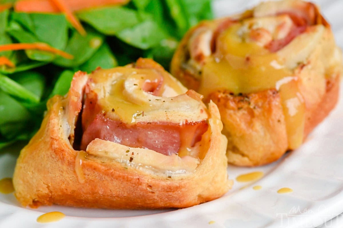 Honey dijon sauce on top of chicken crescent rolls with ham and cheese on a plate in front of a salad.