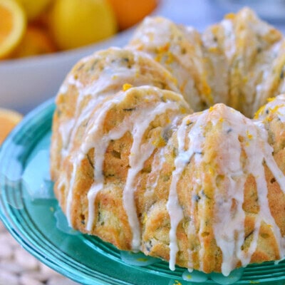 whole zucchini bundt cake topped with orange glaze and sitting on green cake stand.