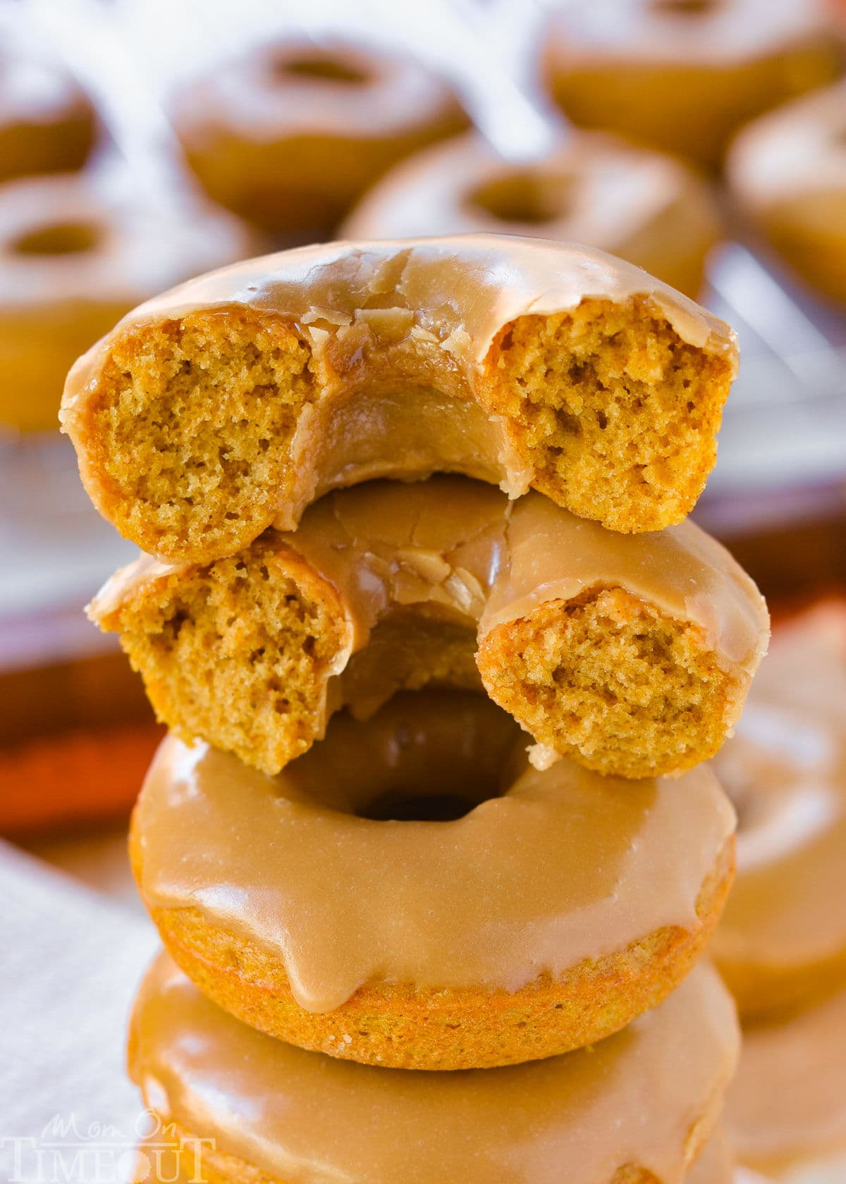 Stack of pumpkin donuts and top donut has been torn in half and stacked showing the moist cake-like interior and maple glaze.