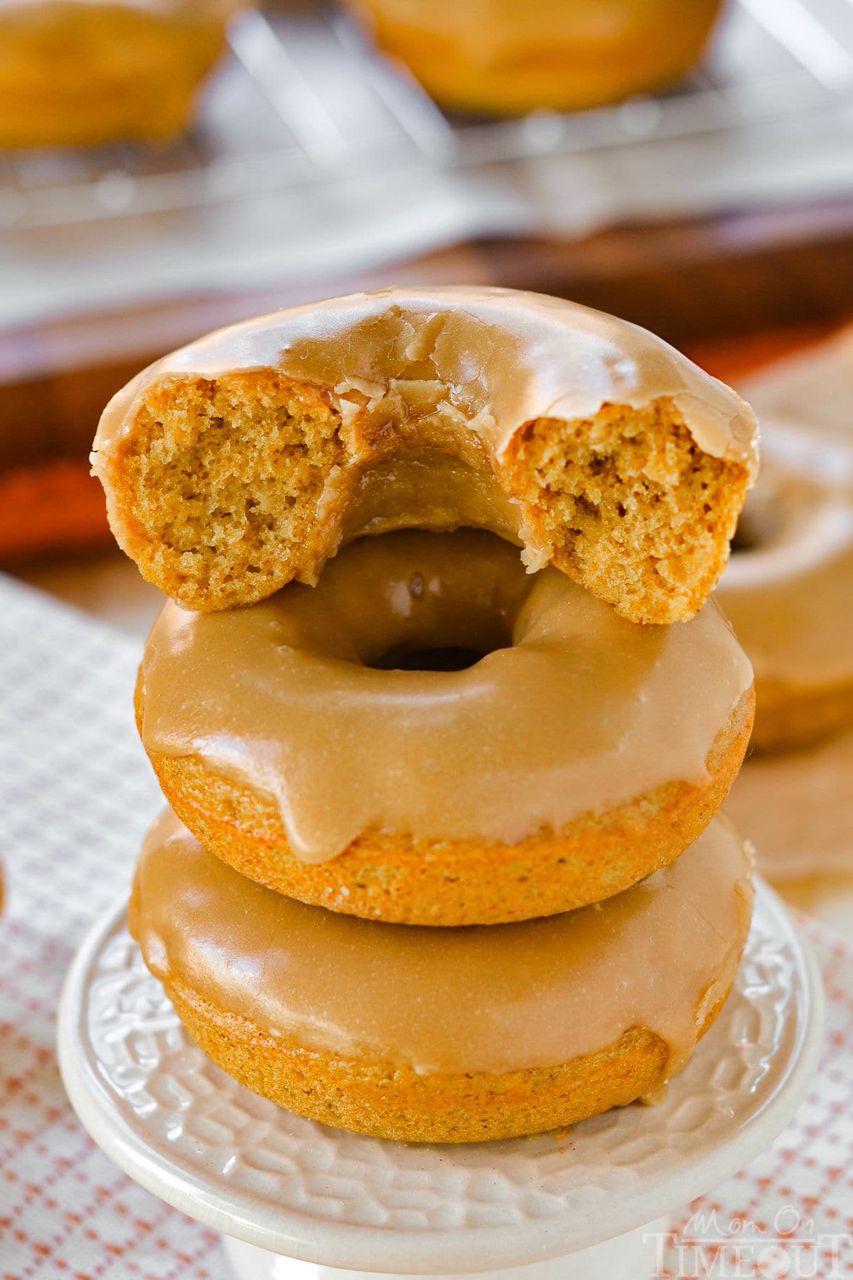 Three pumpkin donuts stacked on cupcake pedestal. Donuts are topped with a maple glaze and half of the top donut is gone. 