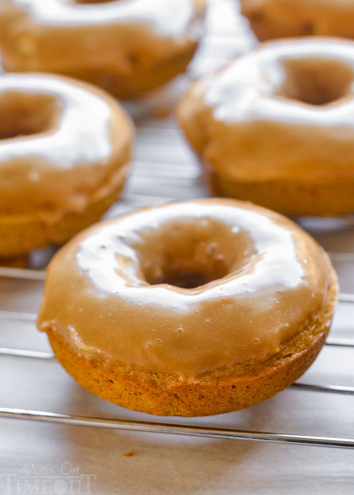 Maple glazed pumpkin spice baked cake donuts sitting on wire cooling rack.