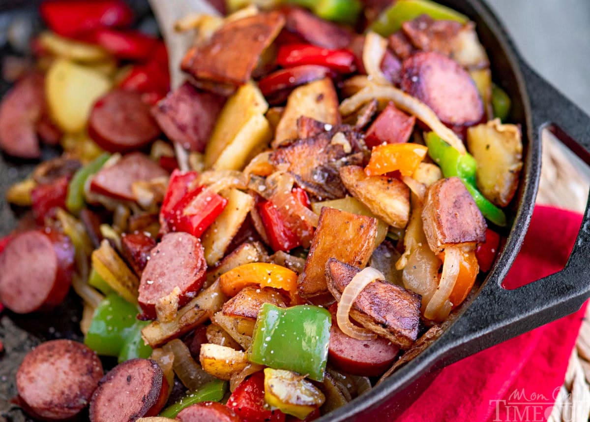 Kielbasa and potatoes in a cast iron skillet ready to be enjoyed. Skillet is resting on a red napkin. Peppers, onions, potatoes and kielbasa are all cut into bite sized pieces.