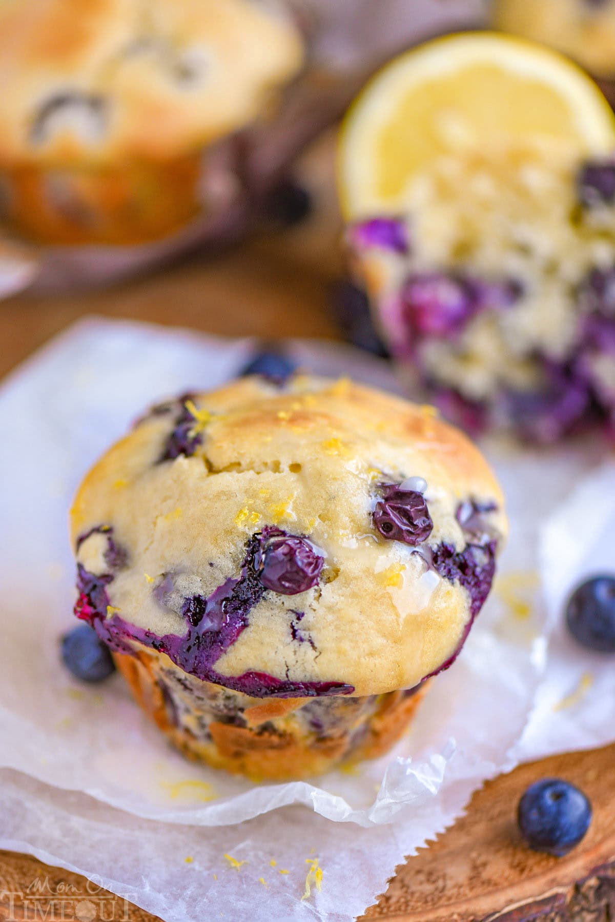 Blueberry Lemon Cream Cheese Muffins topped with a lemon glaze resting on white parchment paper.