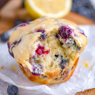 Blueberry muffin made with cream cheese and lemon sitting on white parchment with a bite taken out of the muffin. A lemon half can be seen in the background.