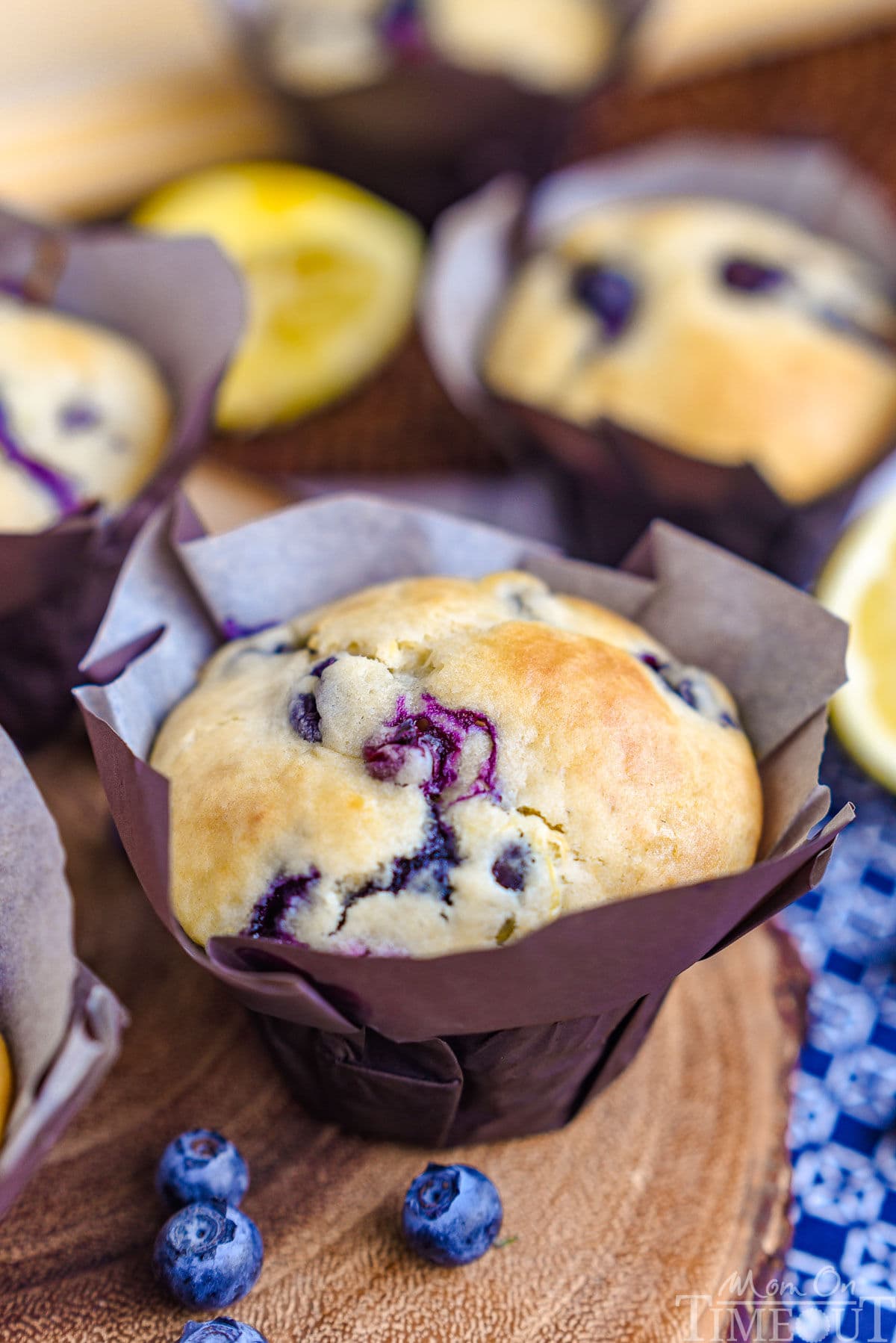 Blueberry Lemon Muffin in a parchment tulip liner sitting on a wood board next to a few blueberries.