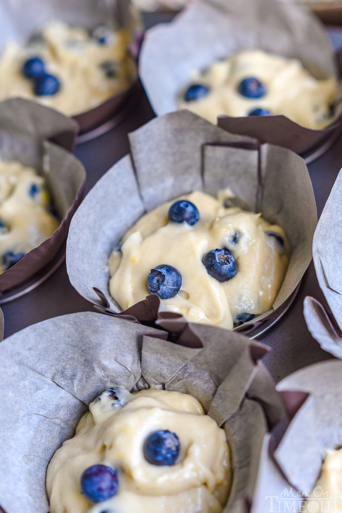 blueberry muffins in muffin tin with batter in tulip parchment liners ready to bake.