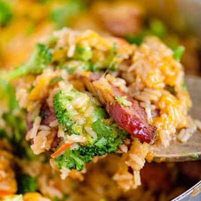 Scoop of cheesy kielbasa broccoli skillet recipe being held over the skillet.