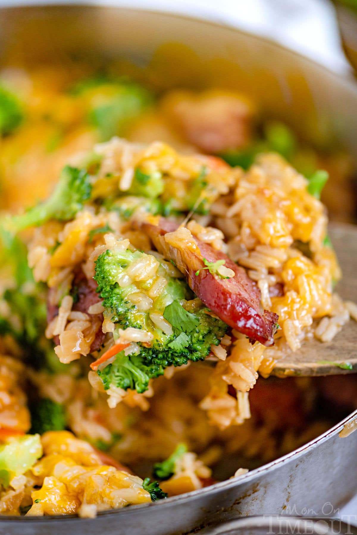 Scoop of cheesy kielbasa broccoli skillet recipe being held over the skillet.