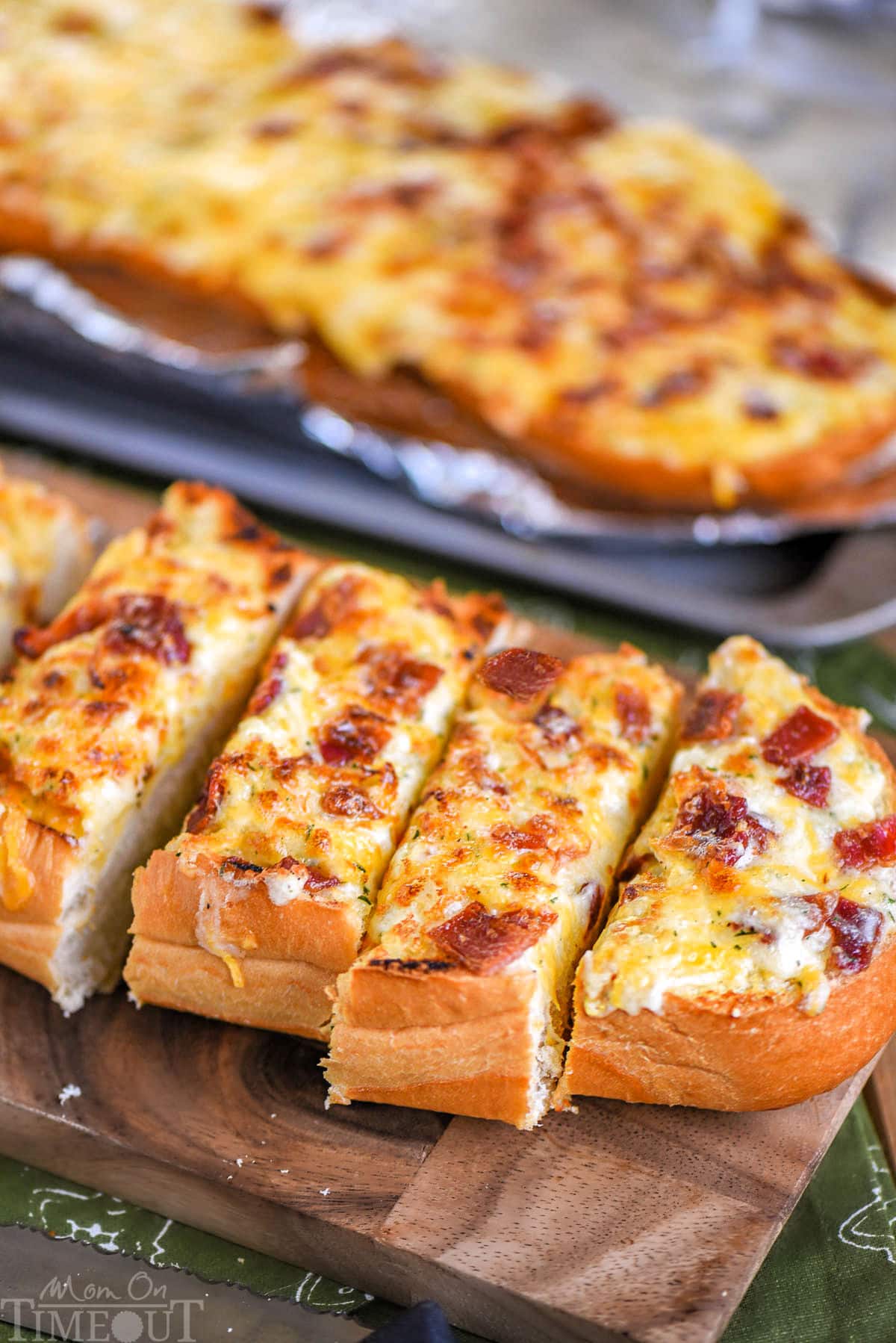 Loaf of cheesy bread made with bacon and ranch resting on wood board cut into pieces ready to be enjoyed.