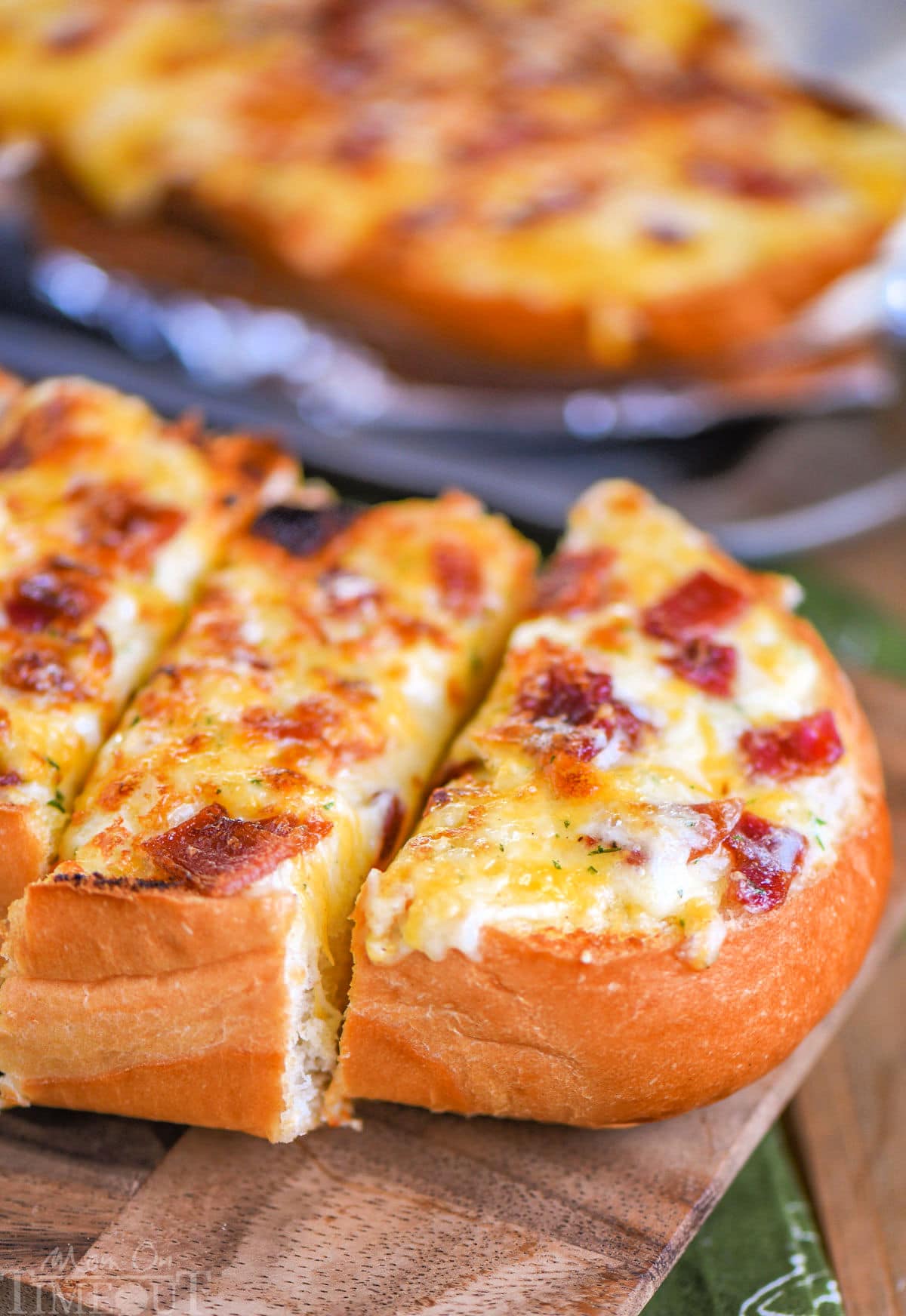 Close up look at loaf of cheese bread made with bacon and ranch. Three pieces have been cut off one half of the loaf on a wood cutting board.