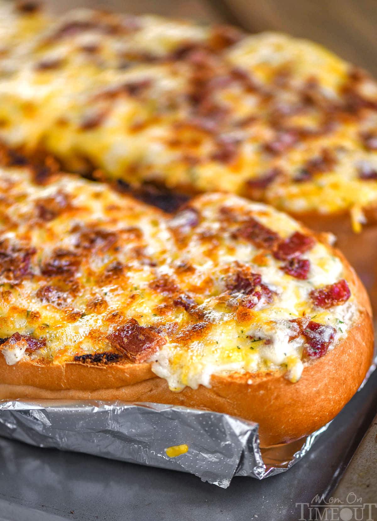 Two halves of a loaf of bread baked up into cheese bread with bacon and ranch. The bread is still on a foil lined baking sheet and has not been cut up.