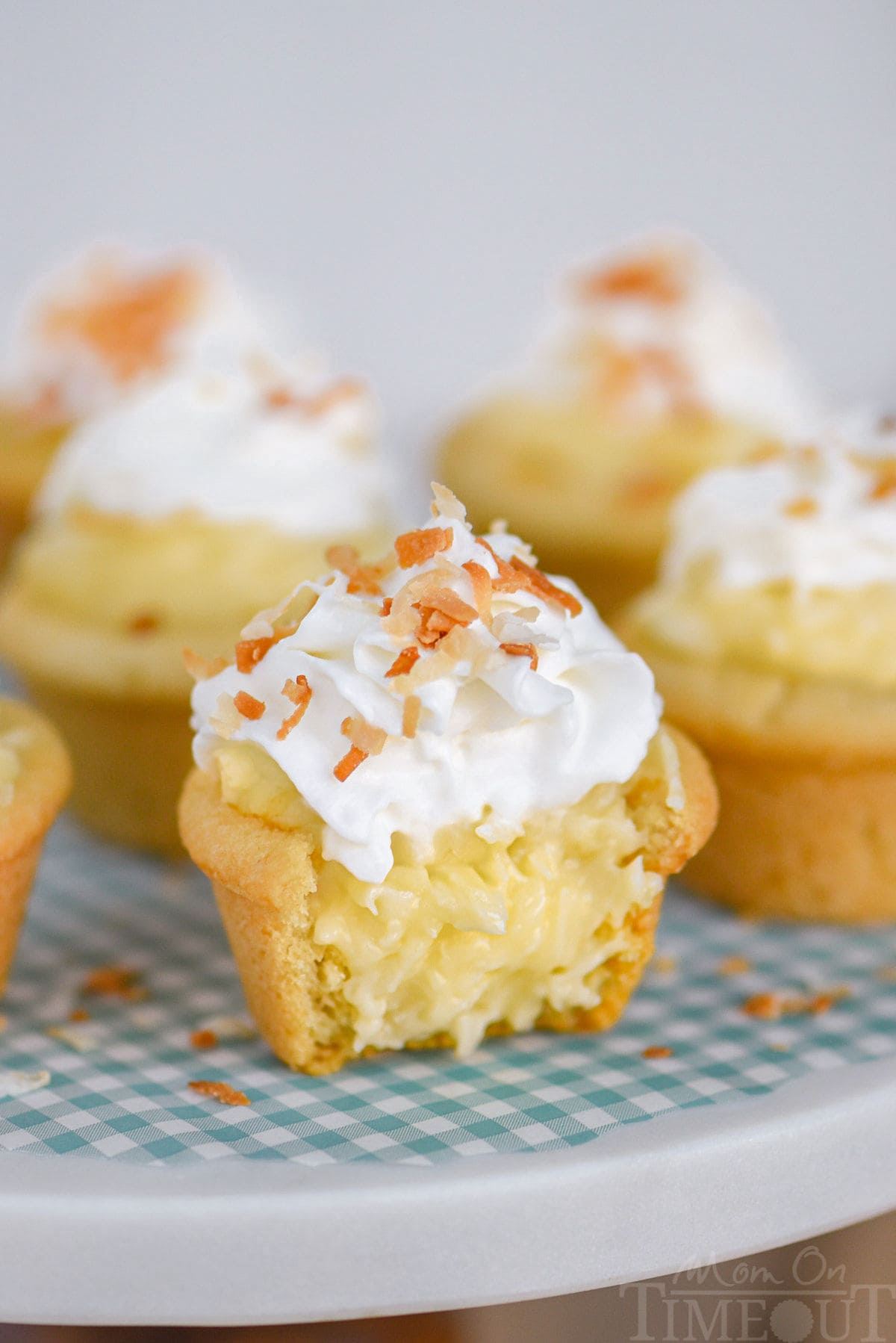 Coconut cream pie cookie cups made with sugar cookie dough are sitting on a marble cake stand and are topped with whipped cream and toasted coconut. The cup in the front has been cut in half.