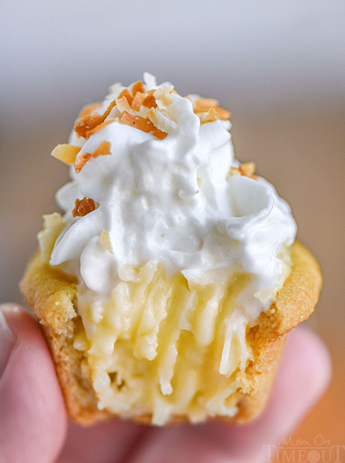 Hand holding up a mini coconut cream pie cookie cup with a bite taken out of it.
