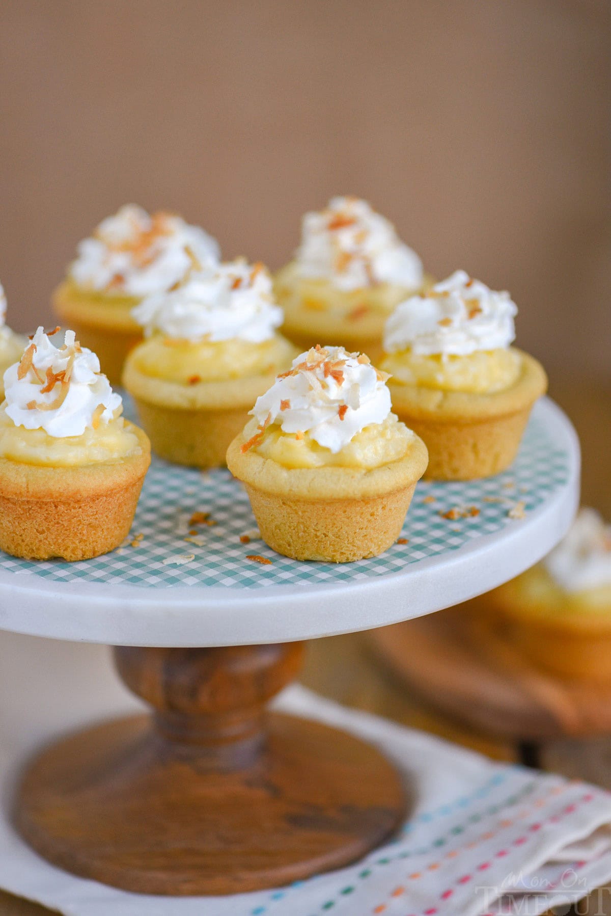 Six mini coconut cream pie cookie cups on a marble cake stand with wood base. 