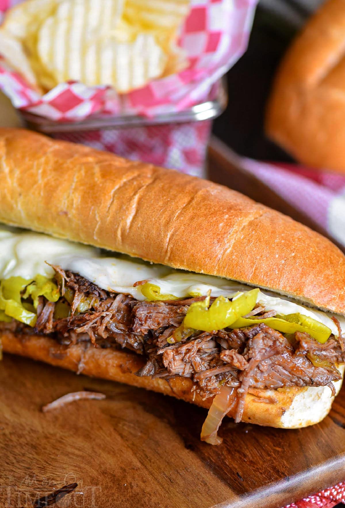 Italian Beef Sandwich sitting on wood cutting board with a basket of chips behind it.