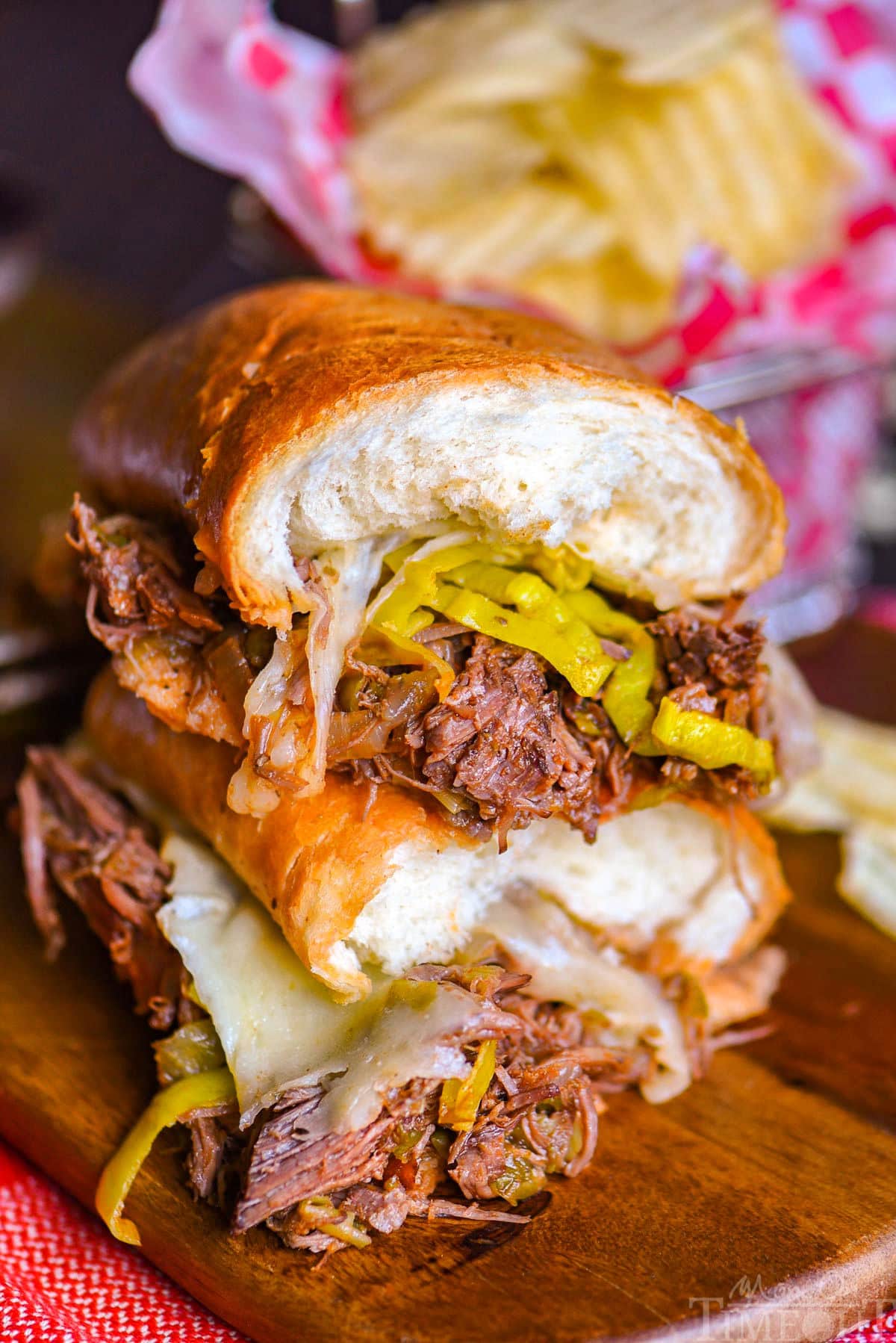 Two halves of a Italian Beef sandwich stacked on top of each other with the melted Provolone cheese and pepperoncinis showing.