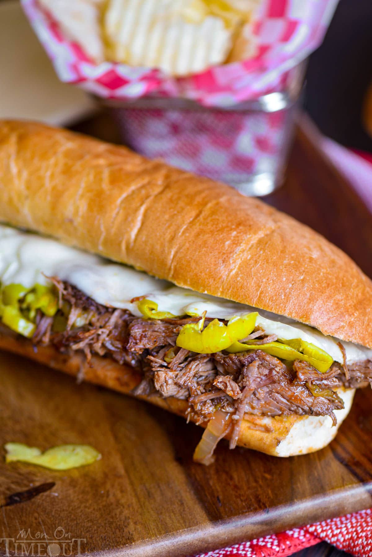 Italian Beef Sandwich recipesitting on wood cutting board with a basket of chips behind it.