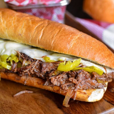 Italian Beef Sandwich sitting on wood cutting board with a basket of chips behind it.