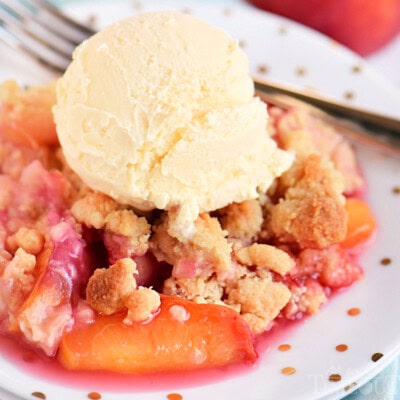 raspberry peach cobbler on white round plate topped with a big scoop of vanilla ice cream.