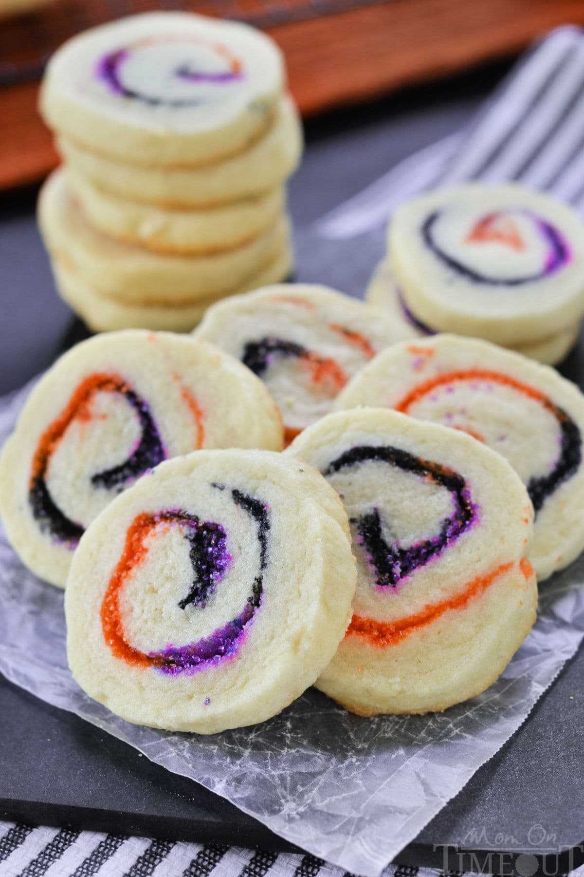 Halloween Sugar Cookies made with orange, black and purple sugar rolleed into a spiral. A stack of cookies in the back and five cookies fanned out in the front to showcase the neat spiral design.