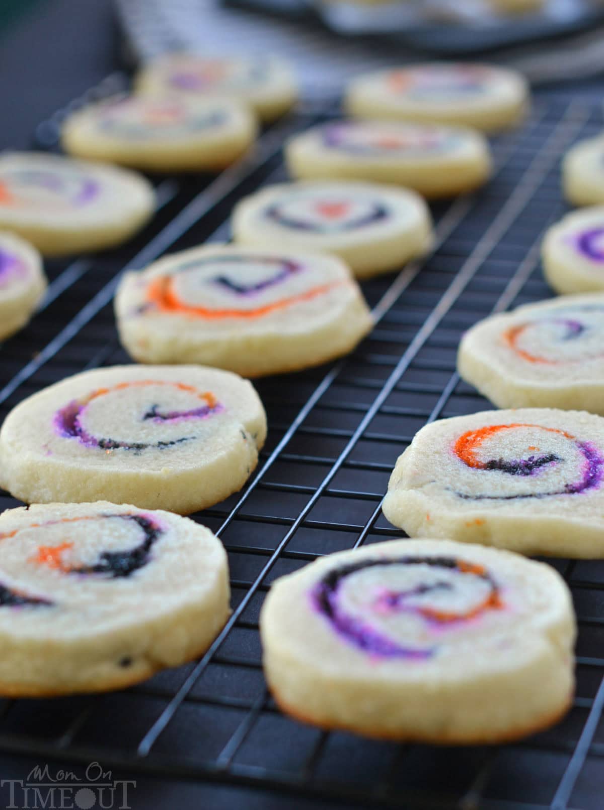 Cookies cooling on black wire rack. Orange, black and purple sugar swirls are clearly visible in the halloween cookies.