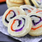 Halloween Sugar Cookies made with orange, black and purple sugar rolleed into a spiral. A stack of cookies in the back and five cookies fanned out in the front to showcase the neat spiral design.