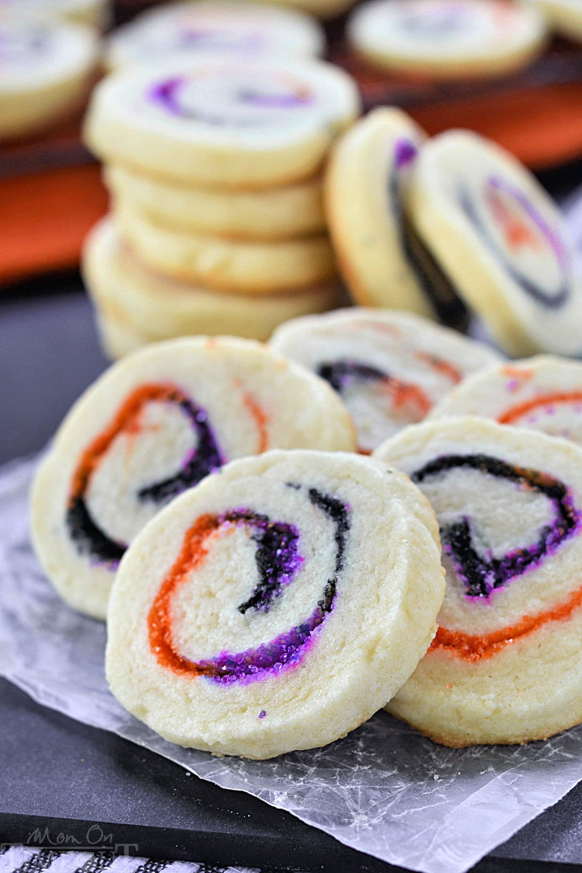 Halloween Sugar Cookies made with orange, black and purple sugar rolleed into a spiral. A stack of cookies in the back and five cookies fanned out in the front to showcase the neat spiral design.