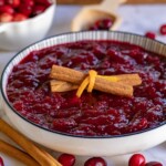 Bowl of slow cooker cranberry sauce ready to be served. Topped with a couple cinnamon sticks.