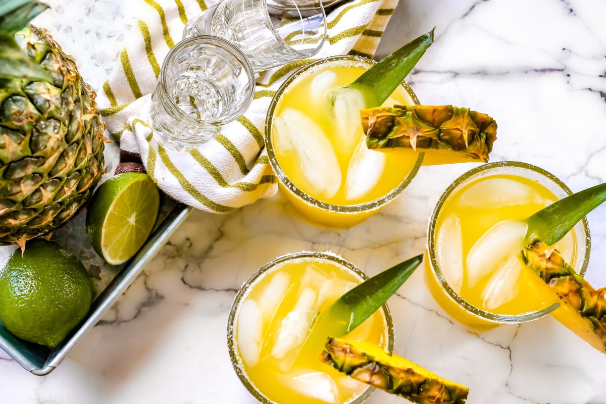 https://www.momontimeout.com/wp-content/uploads/2020/06/easy-pineapple-margarita-recipe-in-glasses-next-to-whole-pineapple-and-limes-on-white-marble-backdrop.jpg