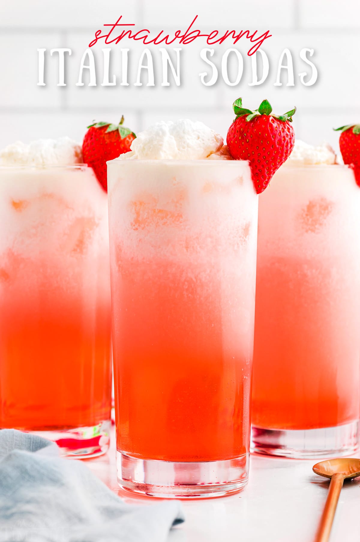 strawberry italian sodas in tall glasses garnished with whipped cream and fresh strawberries. title overlay at top of image.