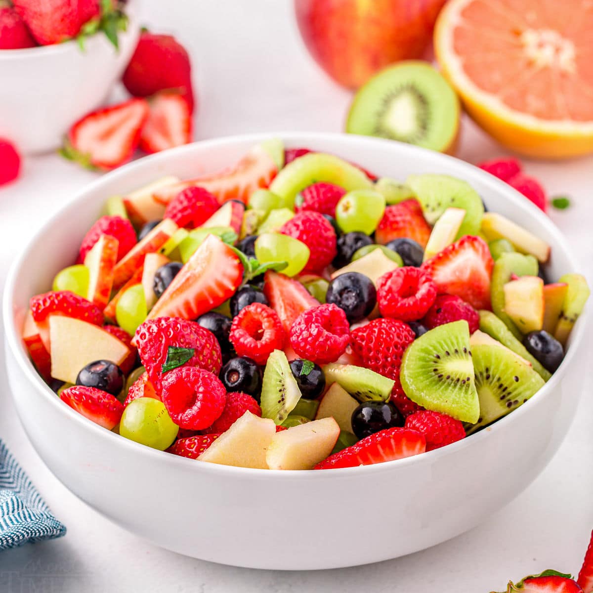 light and refreshing fruit salad with summer fruits in large white serving dish.