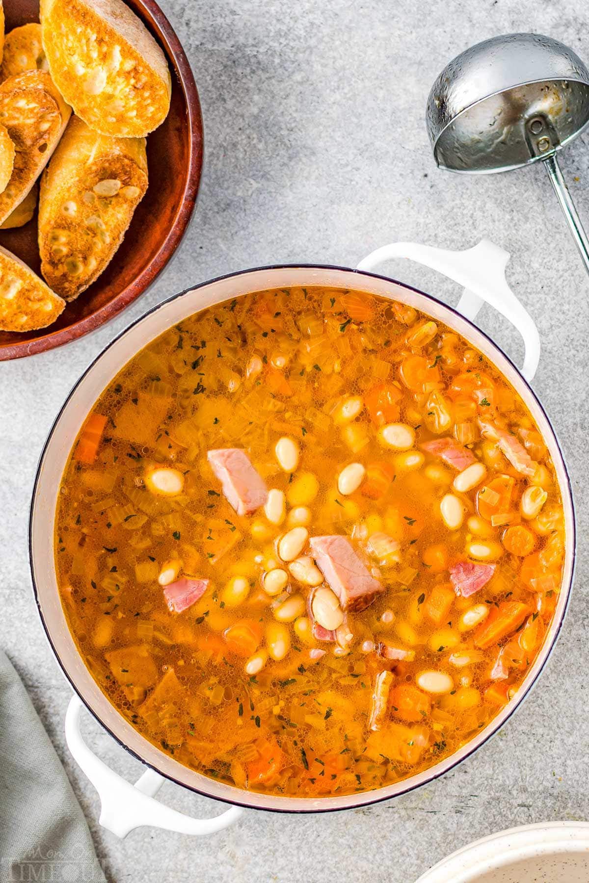 pot full of ham and bean soup with crusty bread in upper left corner on plate.