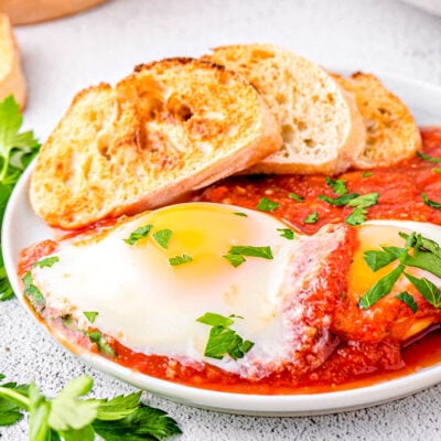 eggs in purgatory plated with extra sauce and nicely toasted crusty bread. The dish is topped with chopped parsley.