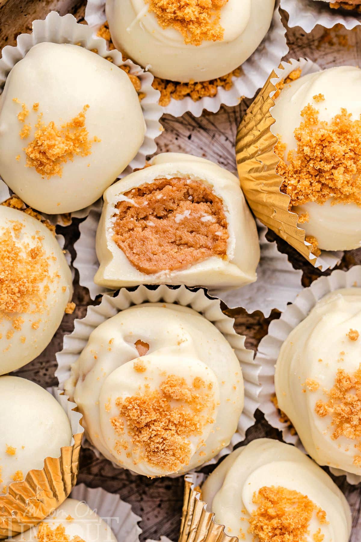 gingerbread truffles in white paper cups with gingersnap cookies crumbles sprinkles on top of the white chocolate coating. one truffle has a bite out of it.