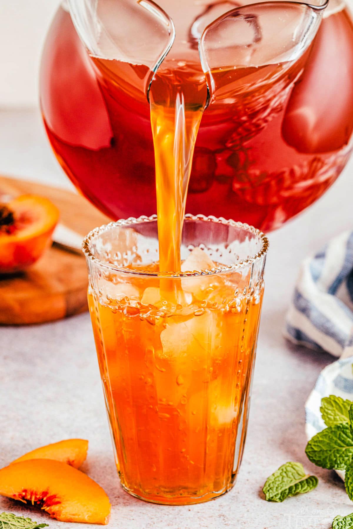 Large pitcher of peach tea being poured into a tall glass with ice.