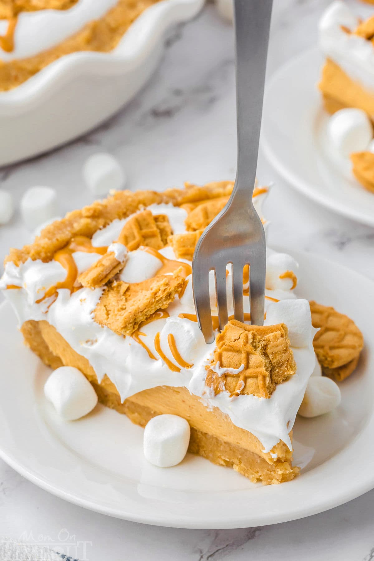 Piece of fluffernutter pie on a round white plate with a fork stuck into the pie. Pie has been topped with peanut butter cookies and marshmallows.