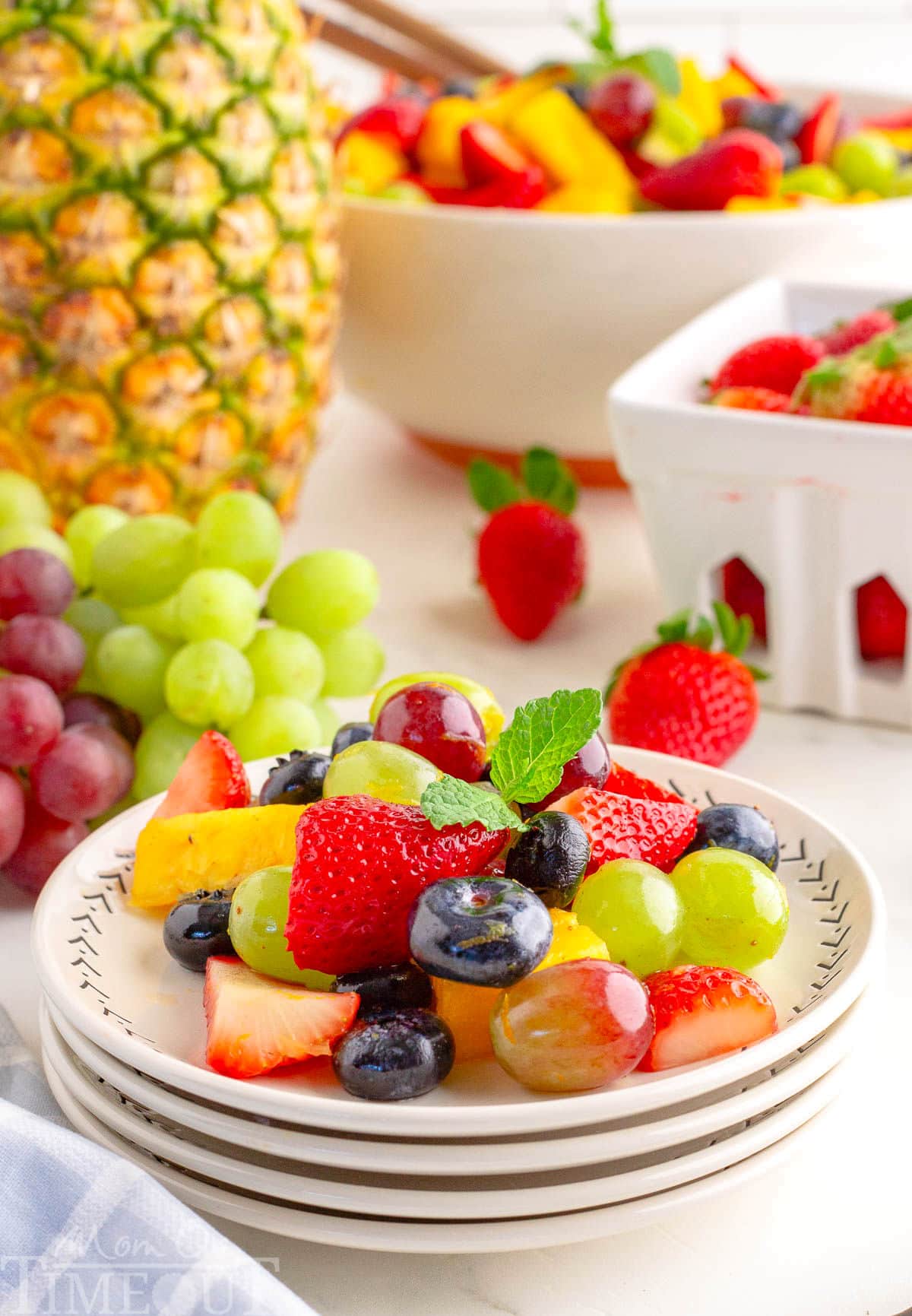 A serving of fruit salad on a white plate with fruit in the background.
