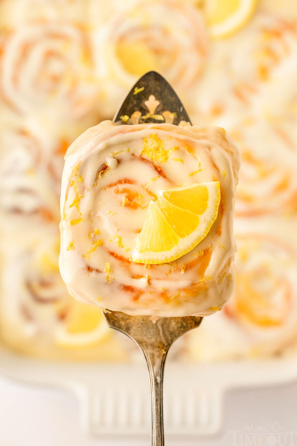 A top-down view of a lemon roll on a spatula, held over the pan of lemon rolls.