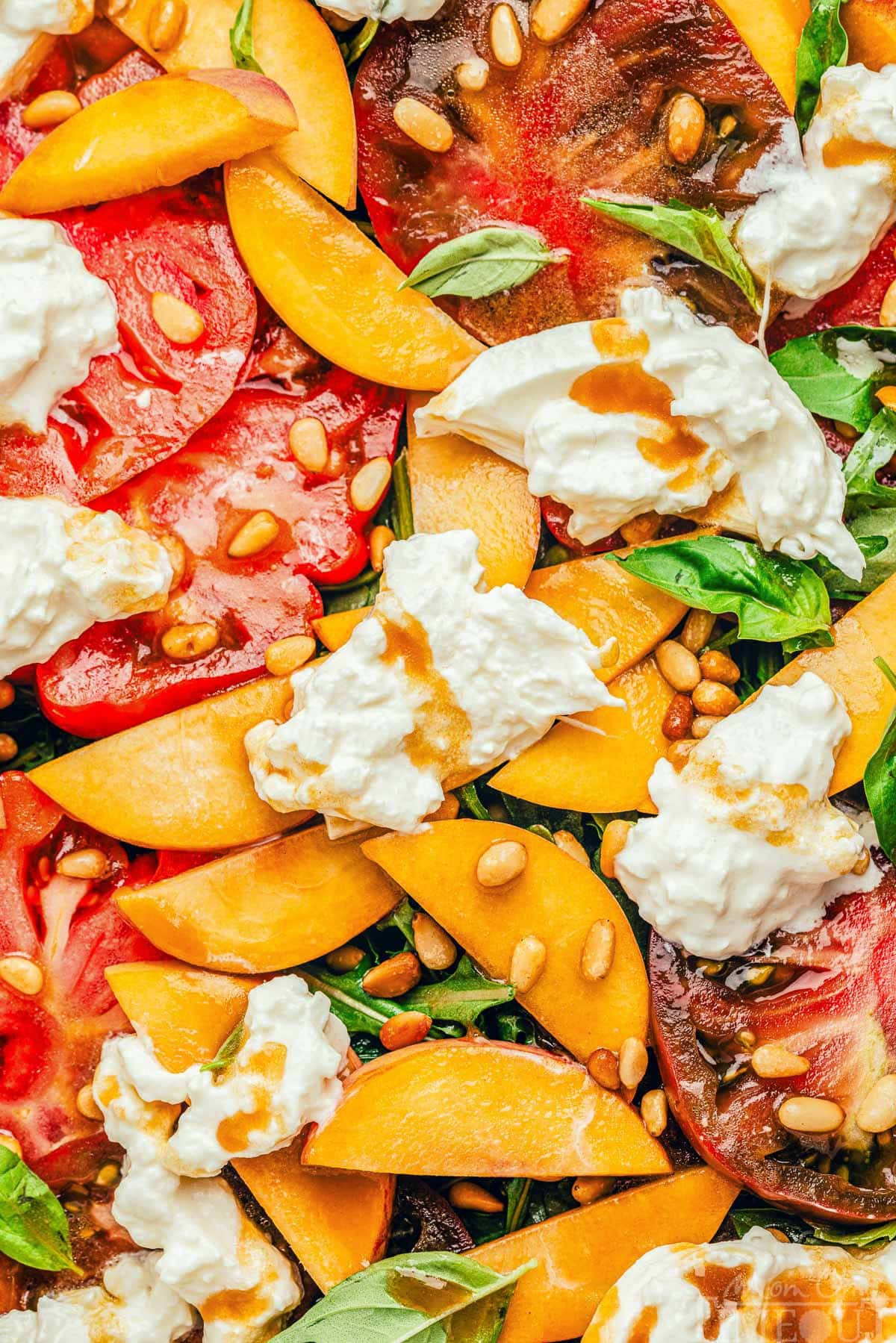 close up of peach tomato salad on a platter. Slices of peaches and tomatoes on arugula topped with burrata cheese and balsamic dressing.