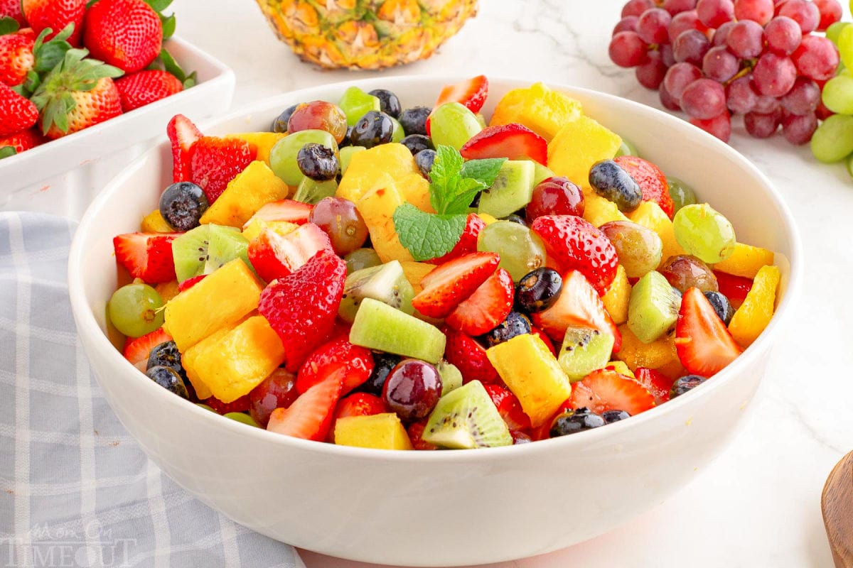 A white bowl of fruit salad made with strawberries, pineapple, blueberries, kiwis and grapes.