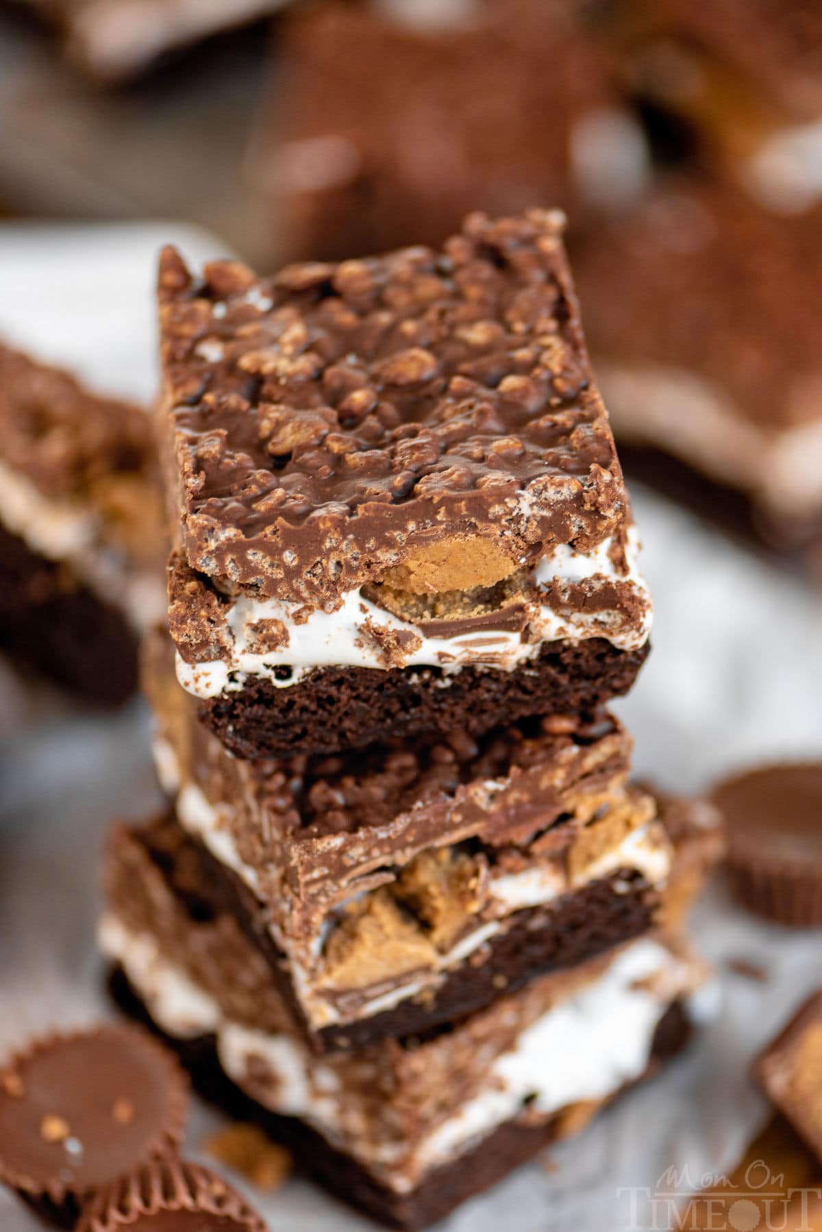 An angled top down view of three brownies stacked on each other with their multiple layers very visible showcasing the marshmallow layer as well as the peanut butter cups.