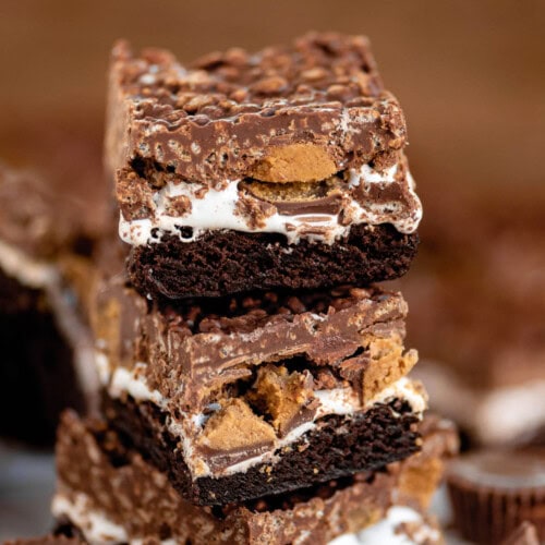 Three brownies stacked on each other so you can clearly see the brownie layer, followed by a marshmallow creme layer, Reese's peanut butter cups and then the top layer which is a chocolate peanut butter rice krispie layer.