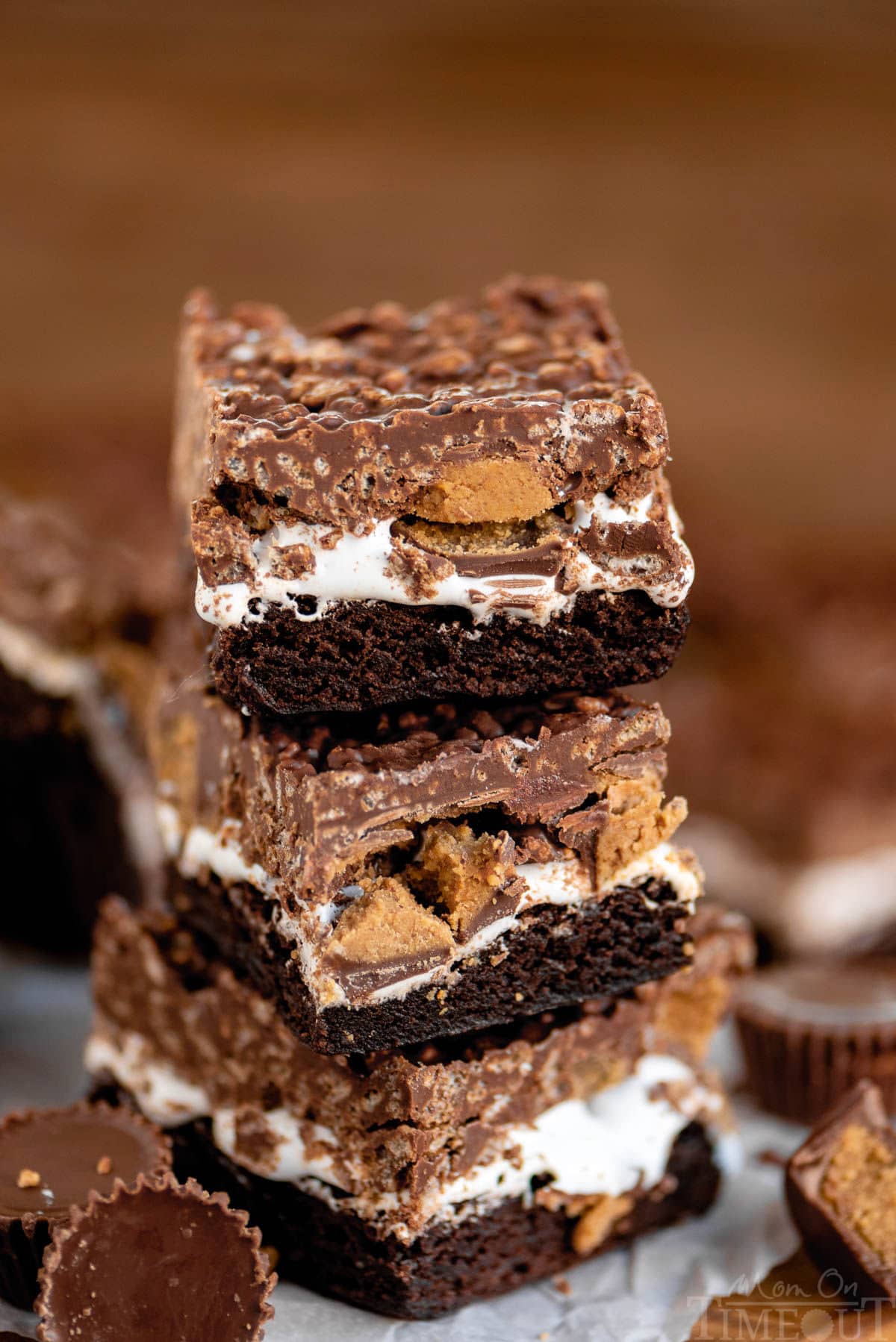 Three brownies stacked on each other so you can clearly see the brownie layer, followed by a marshmallow creme layer, Reese's peanut butter cups and then the top layer which is a chocolate peanut butter rice krispie layer.