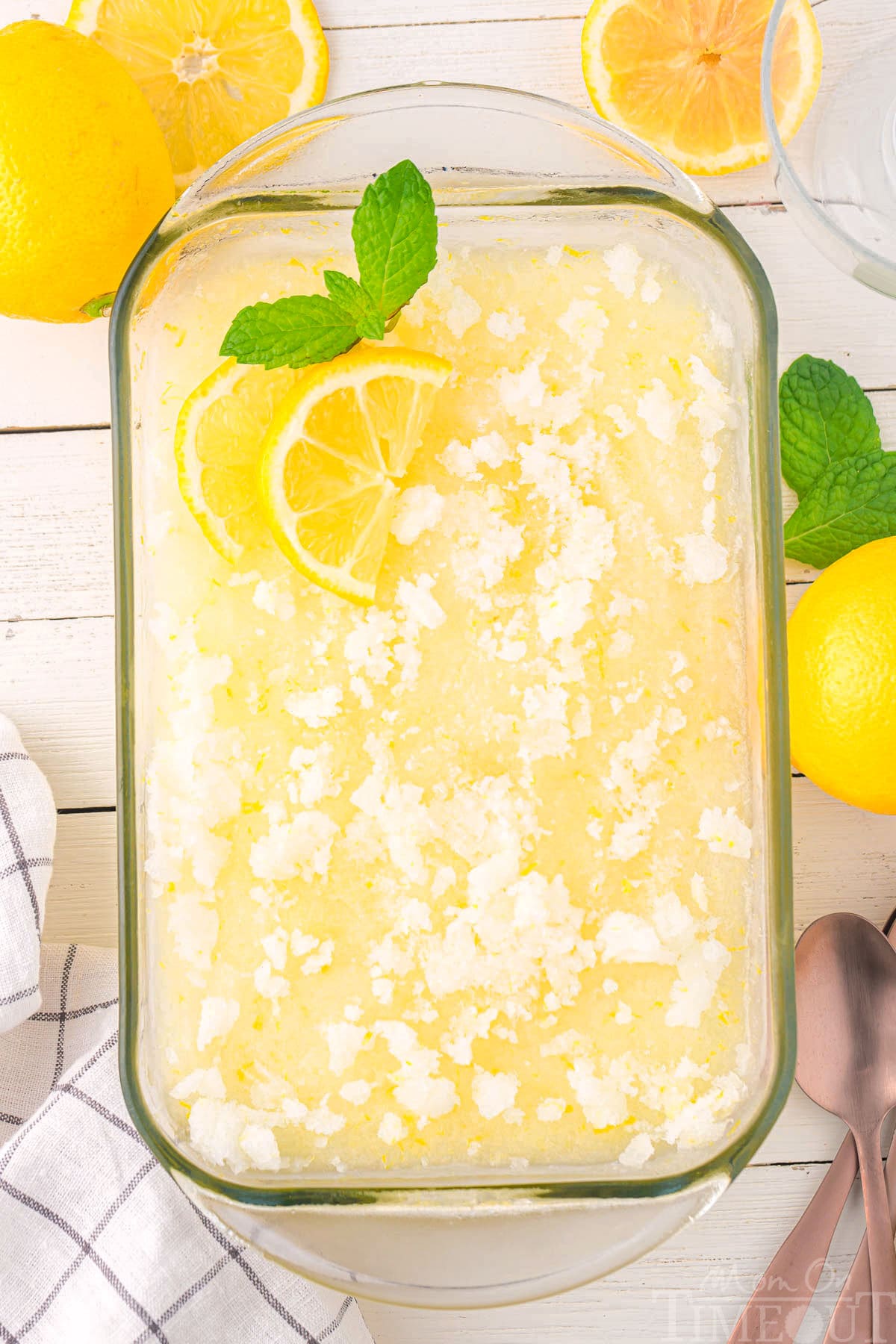 Top down photo of lemon sorbet in a glass pan garnished with lemon slices and a mint leaf.