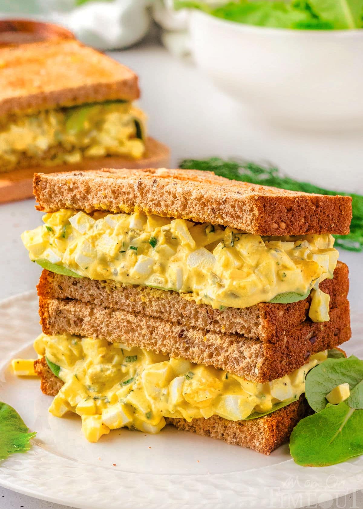 Two egg salad halves of a sandwich stacked on top of each other.