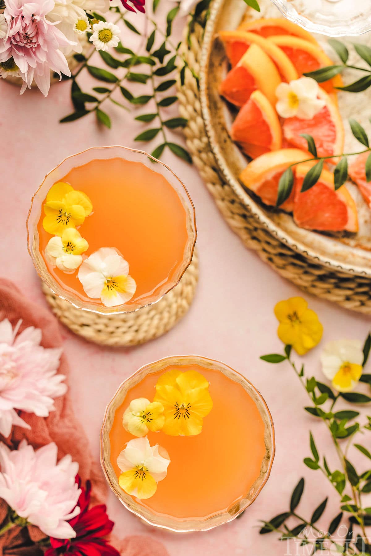 A Top down shot of french blonde cocktails on a pink surface with garnishes.