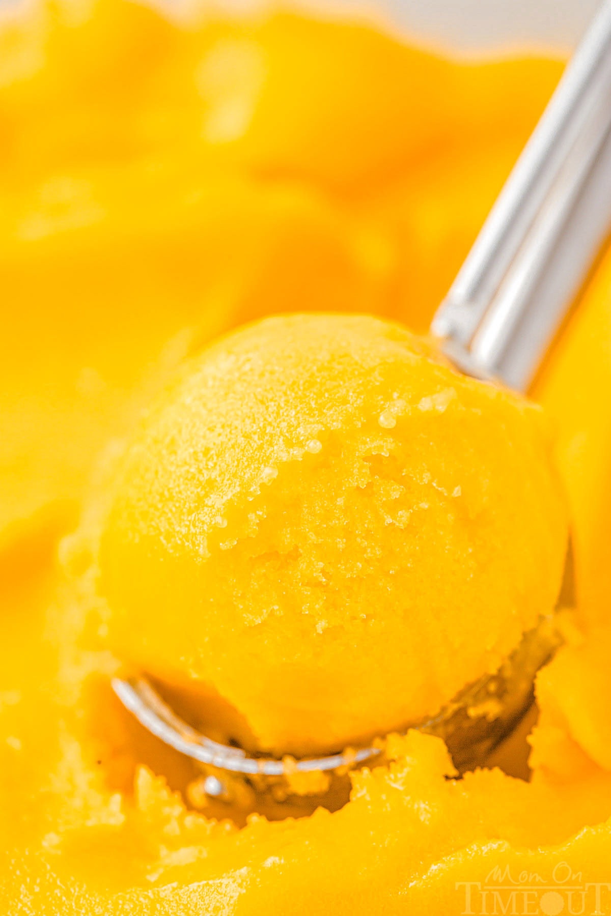 An ice cream scoop scooping mango sorbet.