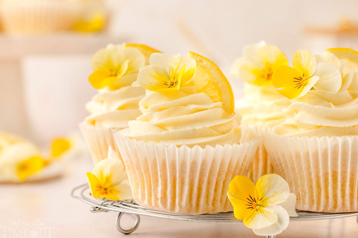 Lemon cupcakes on metal rack frosted beautifully with lemon buttercream and garnished with a small yellow pansies. 