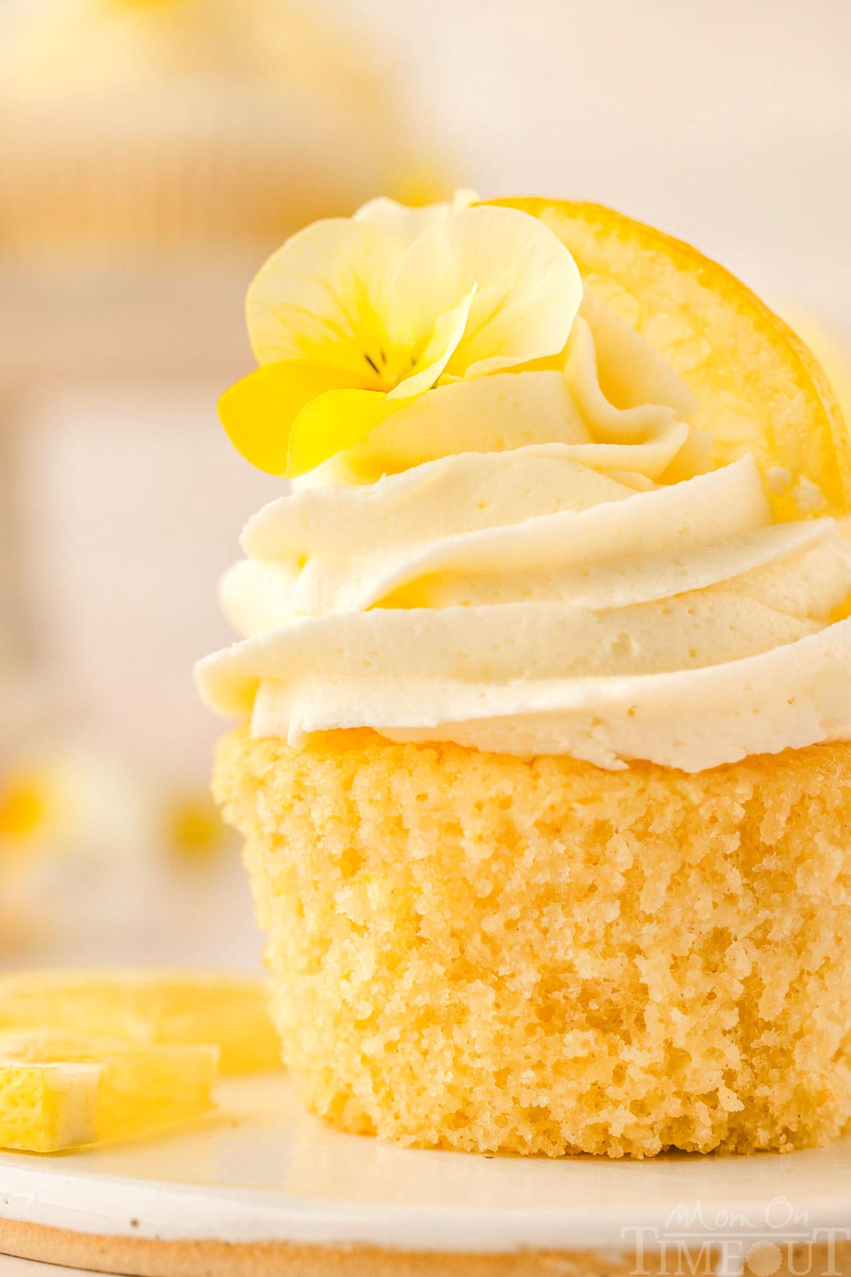 Close up side view of a lemon cupcake with a lemon wedge and flower garnish.