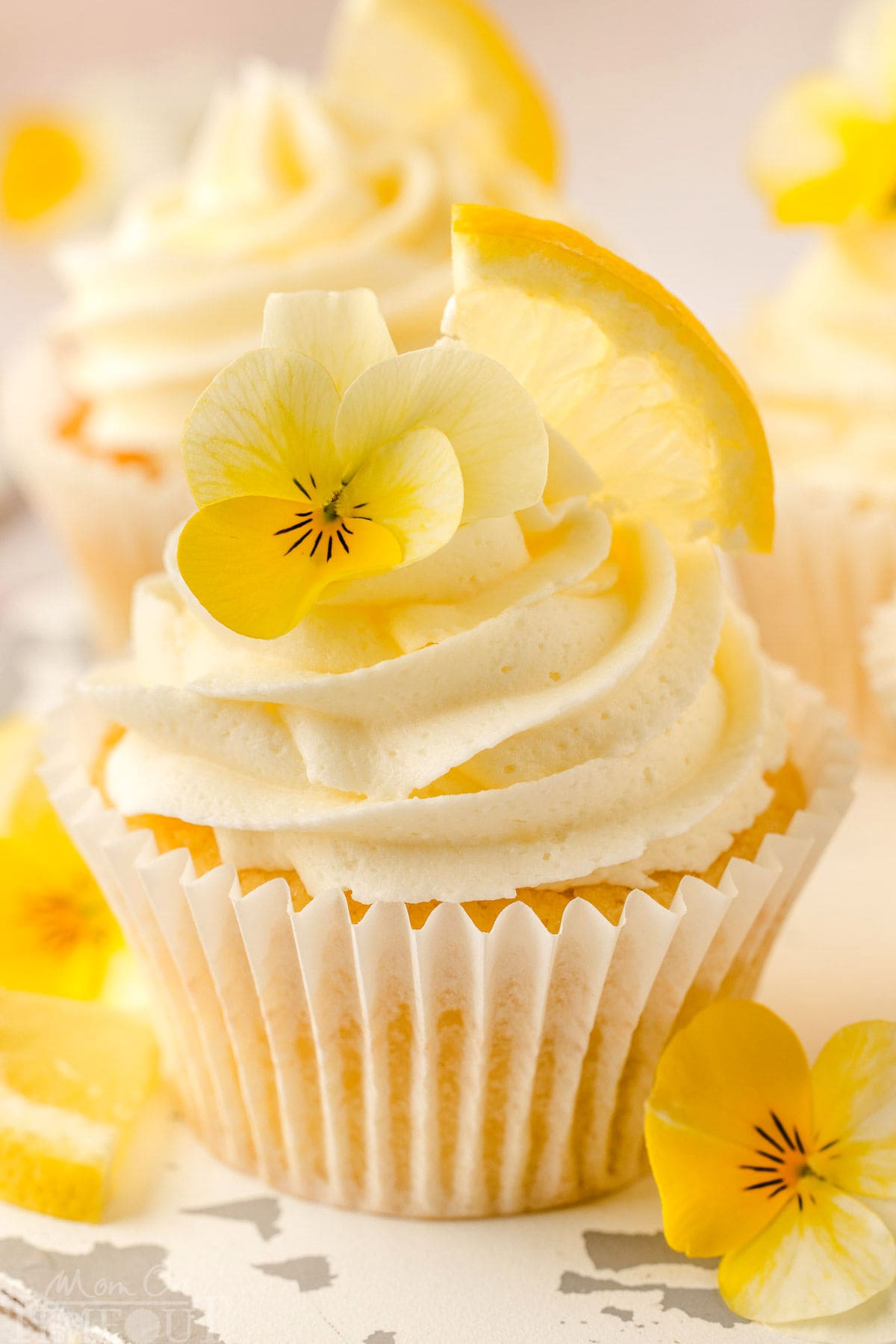 A lemon cupcake with a lemon wedge and flower garnishing it.